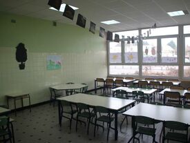 Réfectoire pour les enfants de la maternelle. De grandes fenêtres, pour la clarté. Les tables et chaises sont petites.