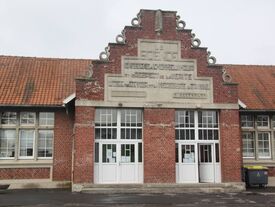 Façade en espalier avec des ornements ronds en ciment. On peut lire une citation de Berthelot : La science enseigne à l'homme l'amour et le respect de la vérité. L'idée du devoir et la nécessité du travail.