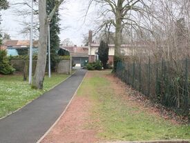 chemin clôturé, en macadam reliant les deux écoles. De nombreux arbres sur les côtés.